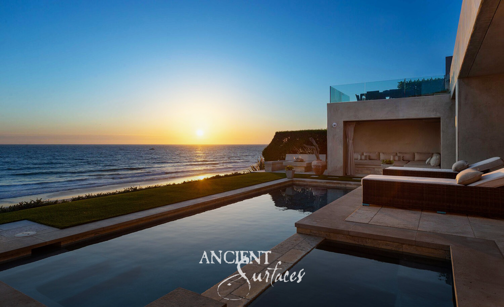 Antique limestone pool terrace above the beach as the sun sets over the open ocean