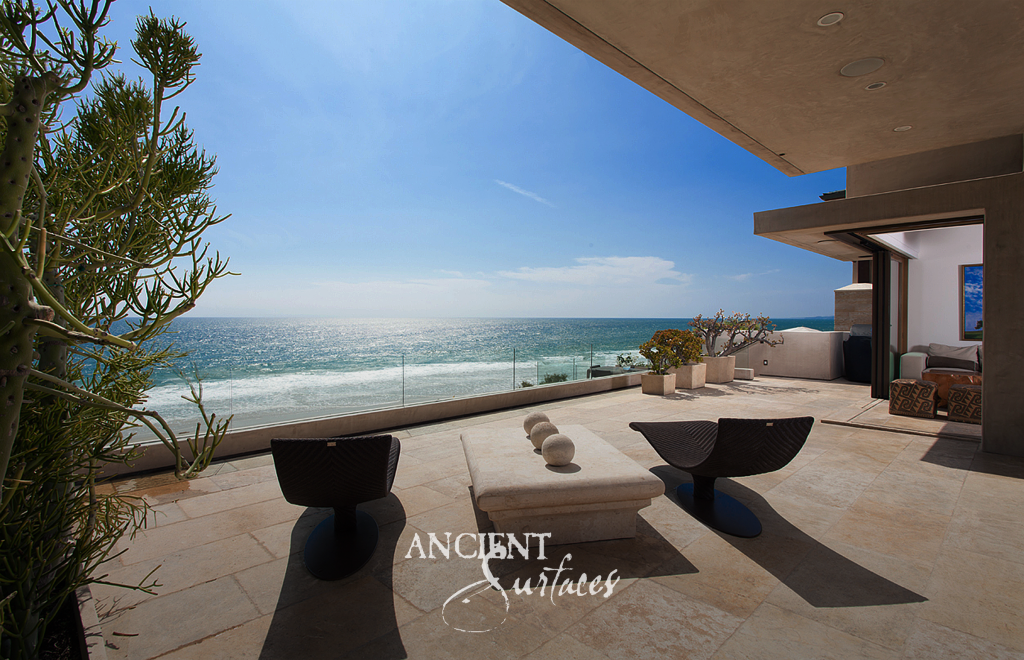 Wide reclaimed limestone terrace with a glass railing looking out across the Pacific
