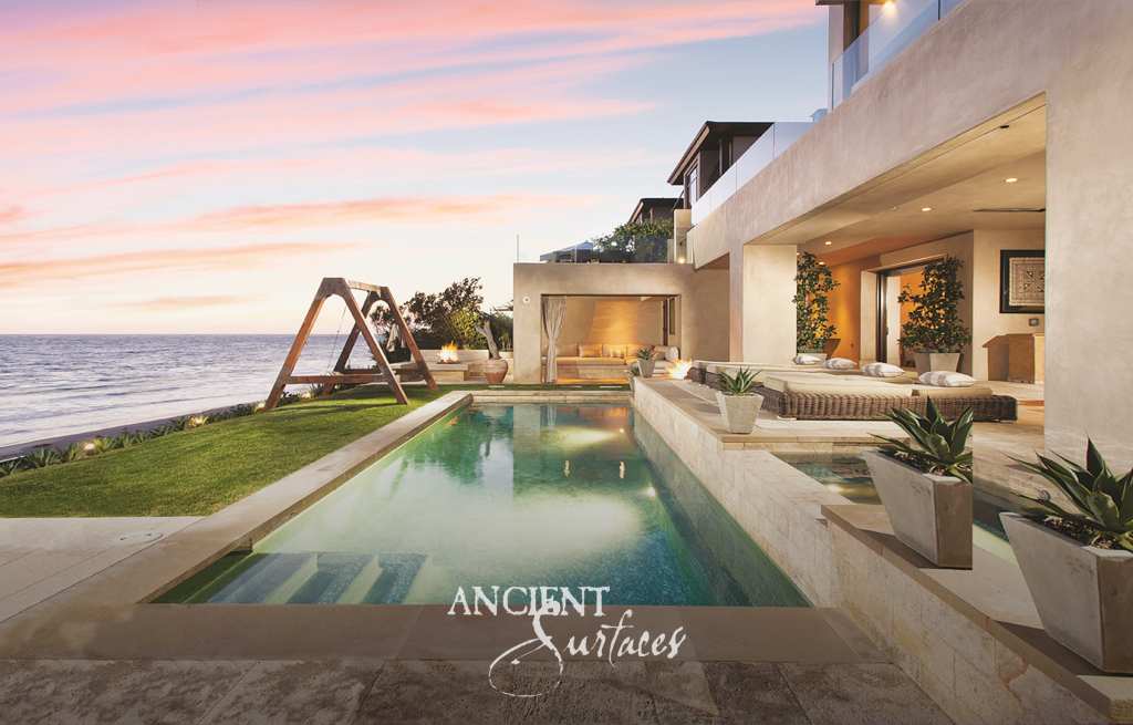Reclaimed limestone pool surround and planted terraces at a coastal residence under a pink evening sky