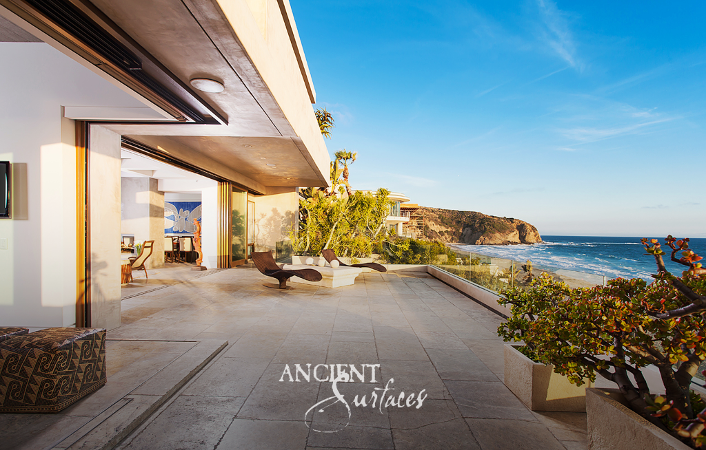 Antique limestone terrace opening off the living room of a coastal residence, with a view along the coastline to the headland