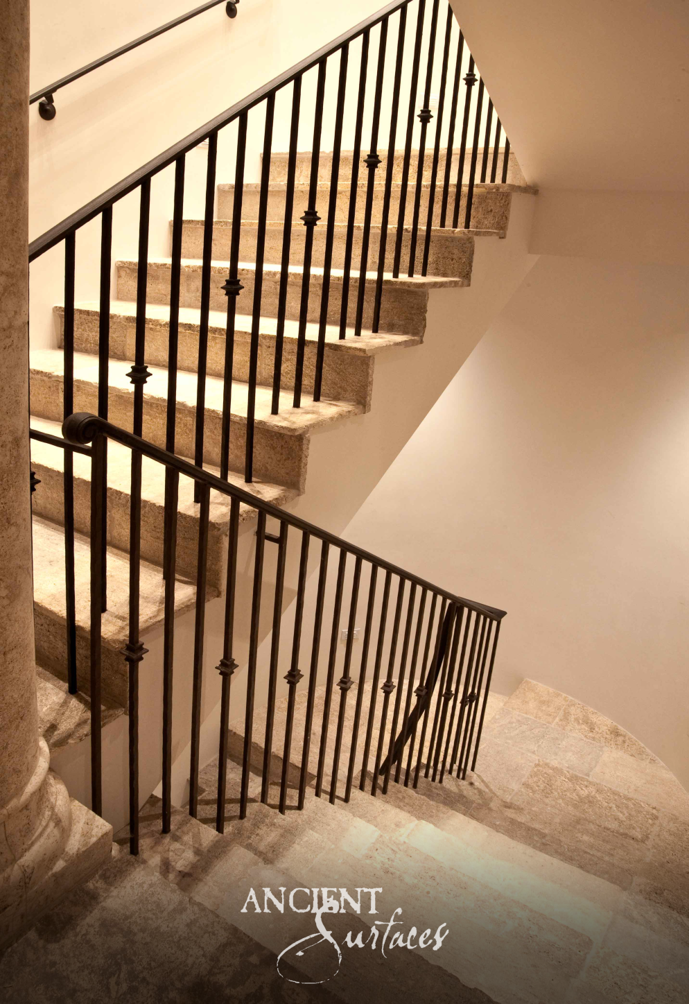 Kronos limestone stair treads with hand dressed edges rising past a slender iron balustrade