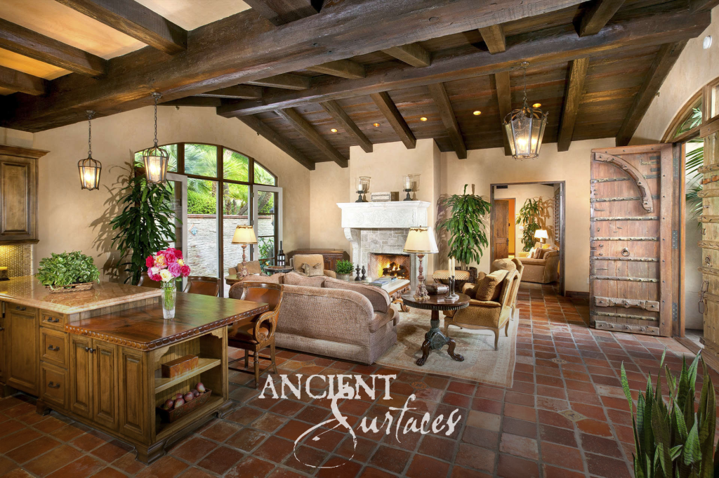 Open plan great room at Puerta Del Sol with antique terracotta floors, dark timber ceilings, a carved limestone mantel, and a studded antique door